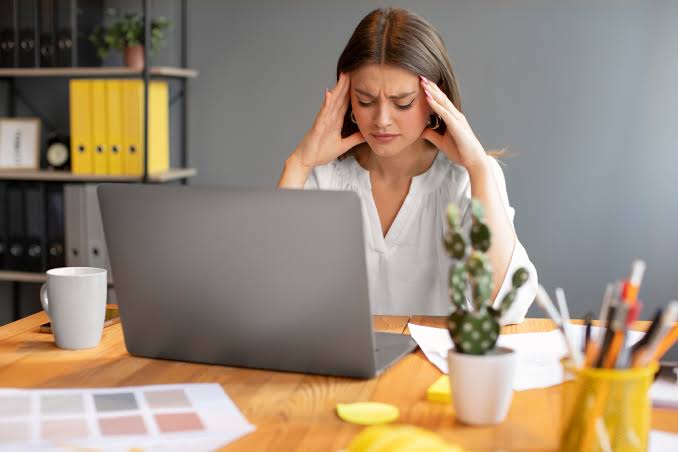 Trabajadora con expresión de estrés frente a su laptop en la oficina